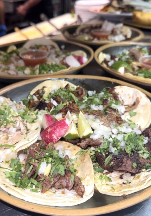 Plates of street tacos with onion, cilantro, radish and lime
