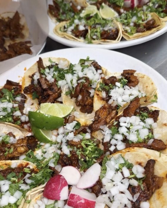 Platter of street tacos topped with onion, cilantro, radish and lime